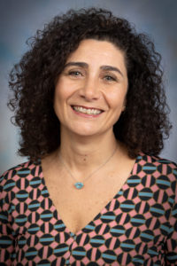 Woman with dark curly hair and a vibrant patterned shirt
