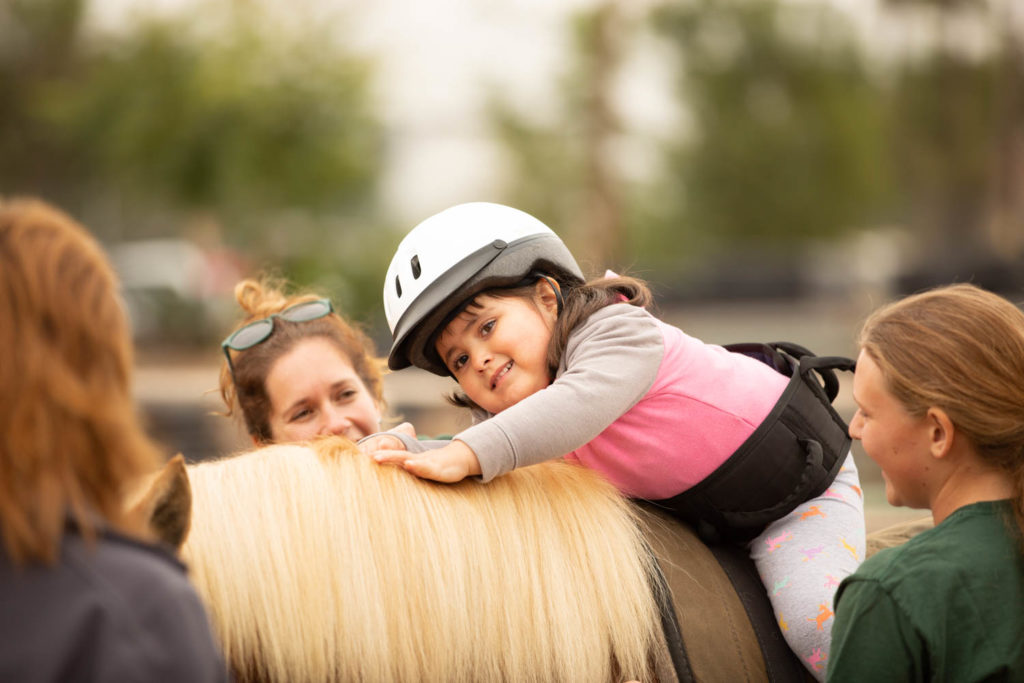 Young girl wearing a helmet riding a horse with three helpers