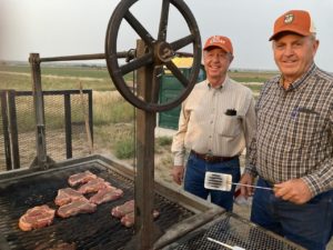 Two men grilling steaks and wearing orange hats
