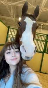 Young woman with brown hair taking a selfie with a horse