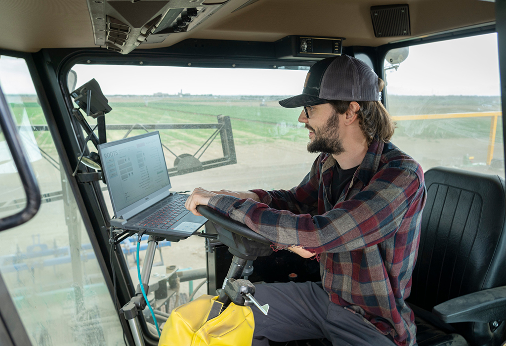 person drives combine while looking at laptop