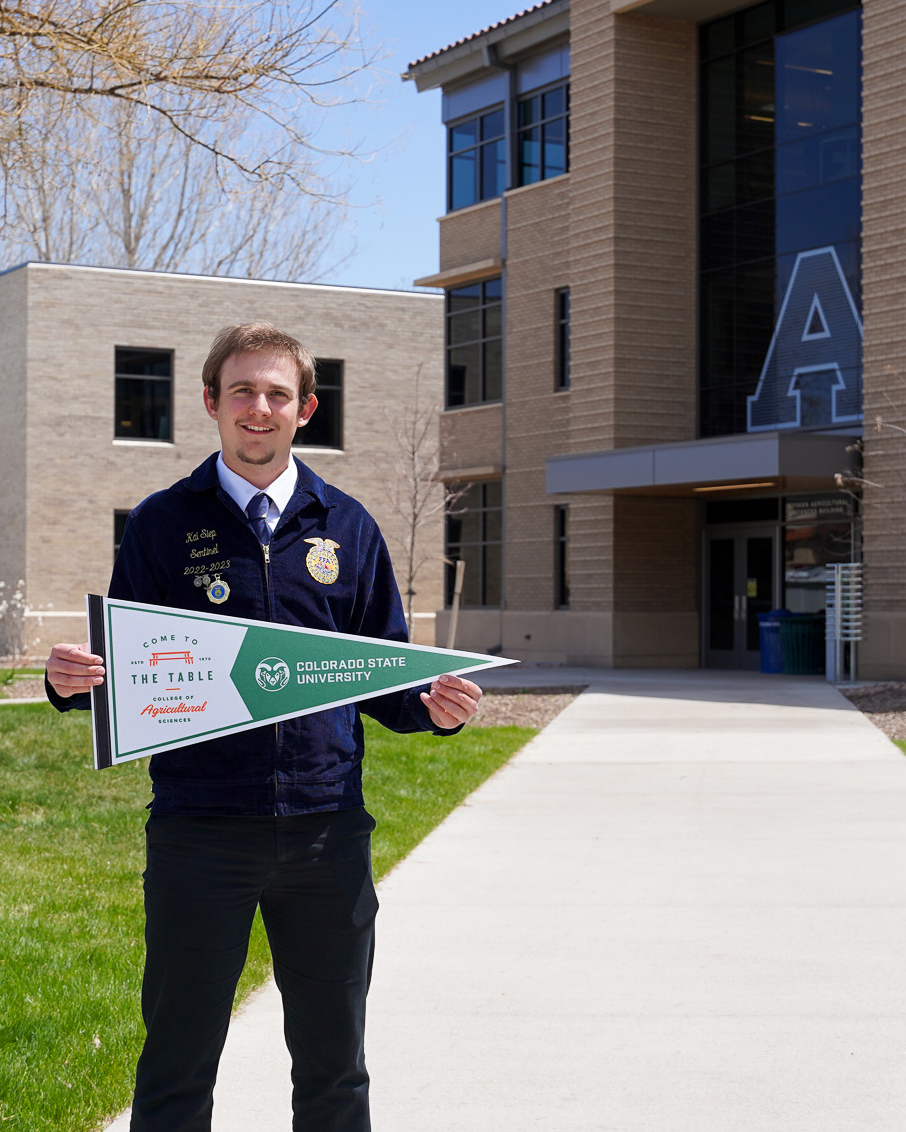 Kai Siep stands in front of the Nutrien Agricultural Sciences Building holding a CSU pennant.